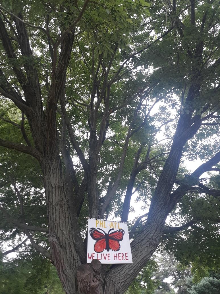 A banner in a tree reads "PHL to ATL, WE LIVE HERE" with a monarch butterfly in the middle.