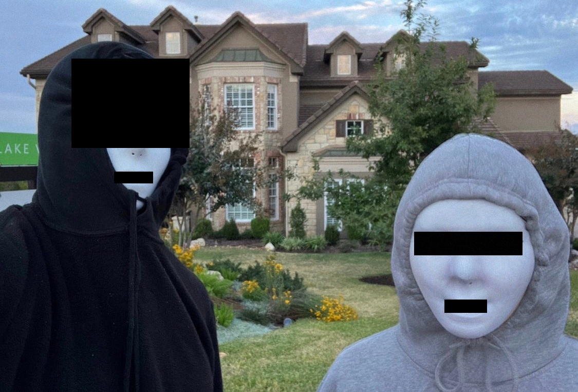 Two people in hoodies wearing white masks stand in front of a McMansion style house.