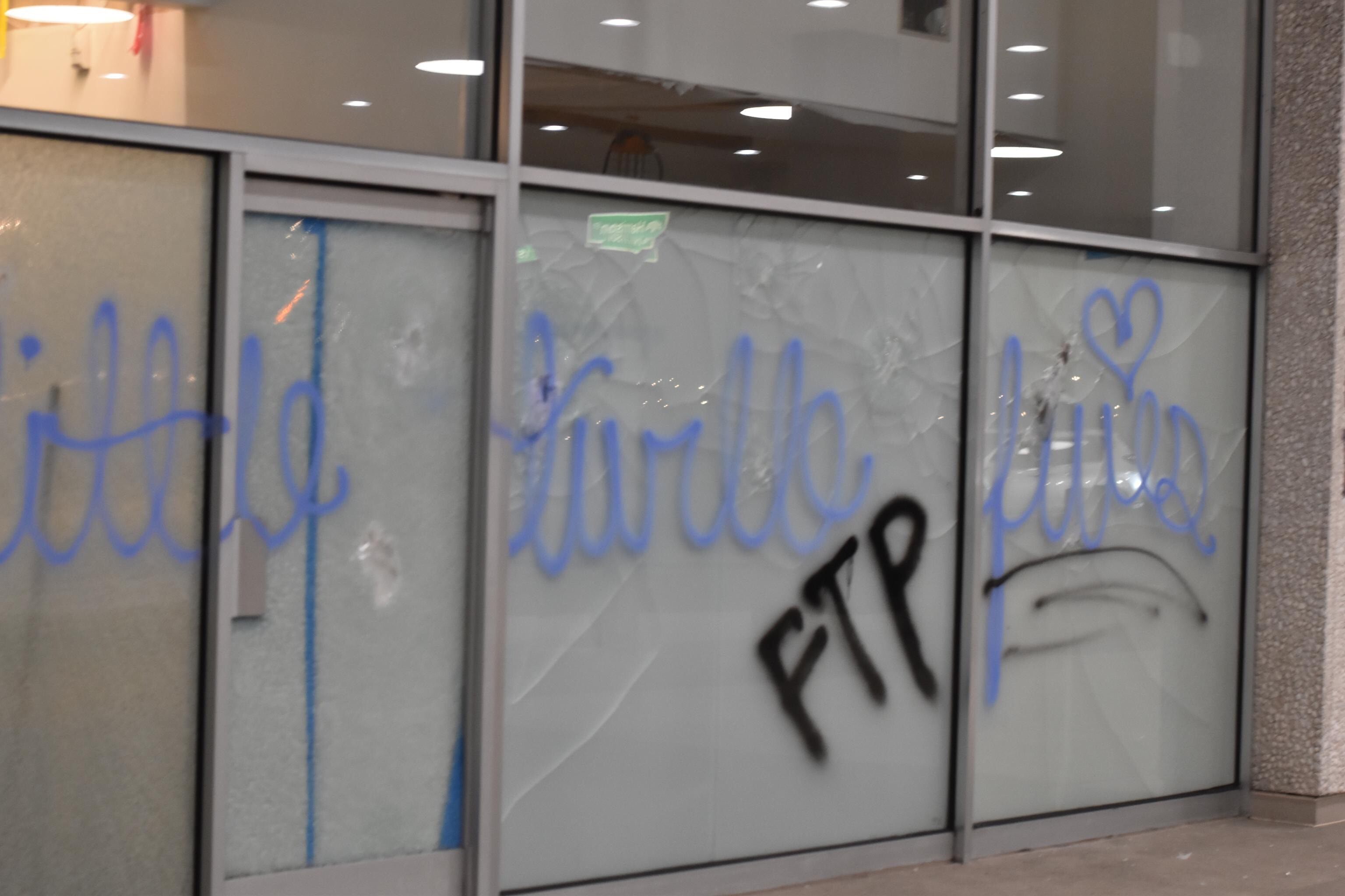 Onto a glass door and several windows, "Little turtle lives" is tagged in light blue spray paint. "FTP" is tagged in black spray paint directly below it.