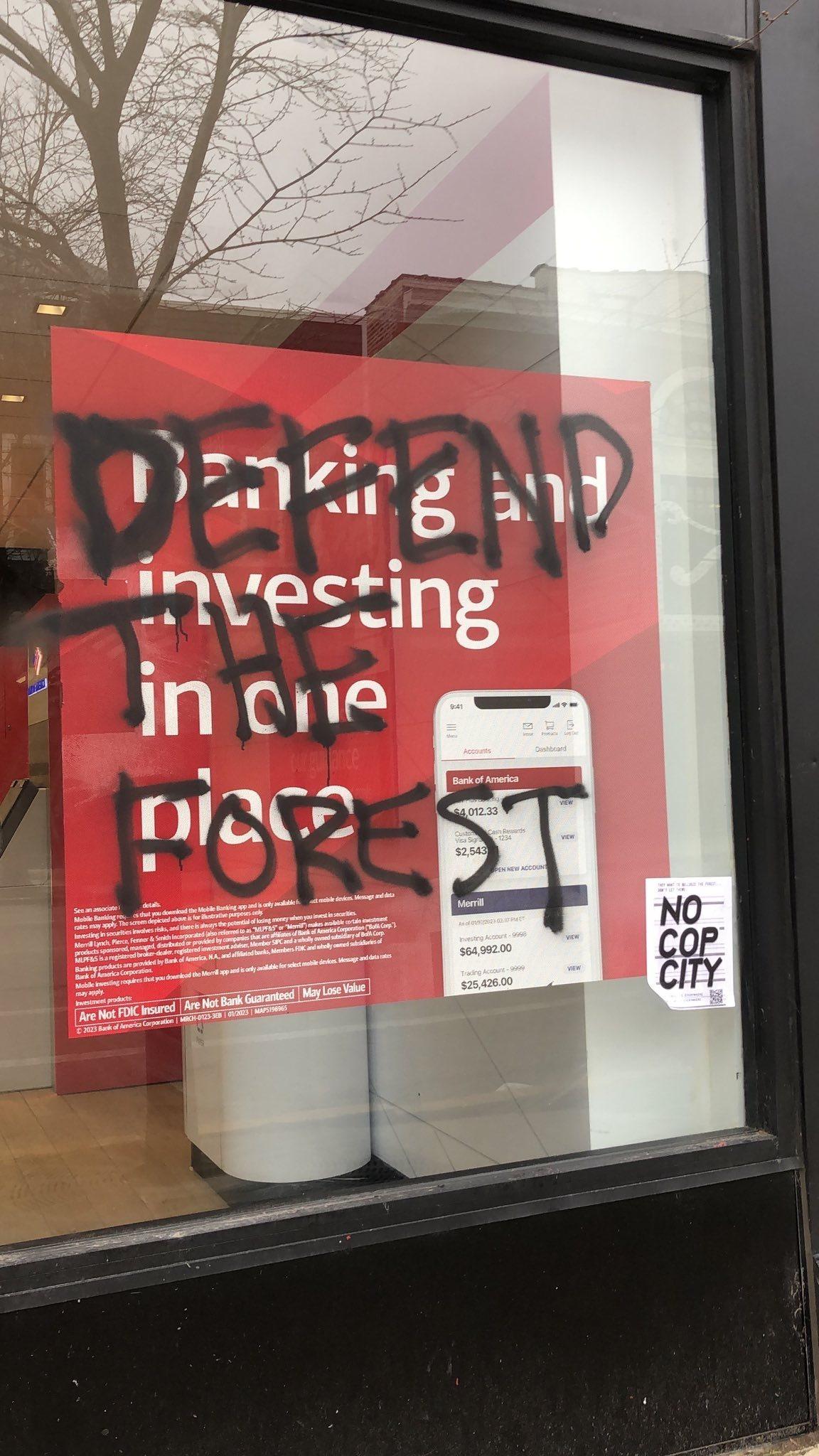 A window with marketing material for Bank of America's stupid app is covered in a tag that says "DEFEND THE FOREST" in black spray paint.