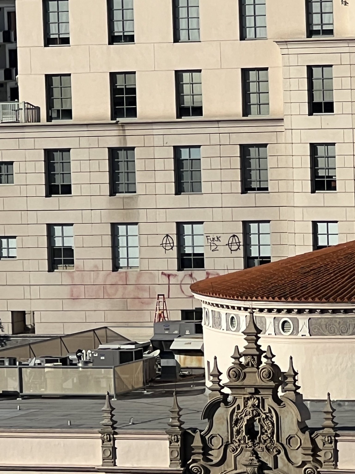 "B&G! STOP COP CITY" is sprayed on the side of a building with several windows in red spray paint. The words are accompanied by several anarchist circle-A symbols, and "fuck 12" is spray painted above it in black spray paint.