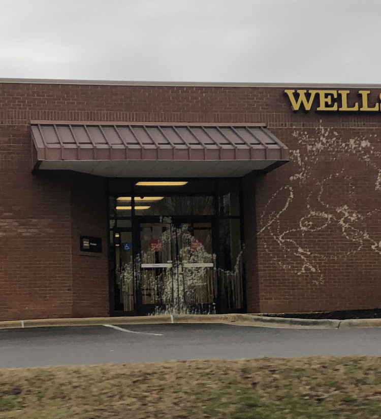 Two glass doors with wells fargo logos and a brick wall are absolutely covered in splattered paint.