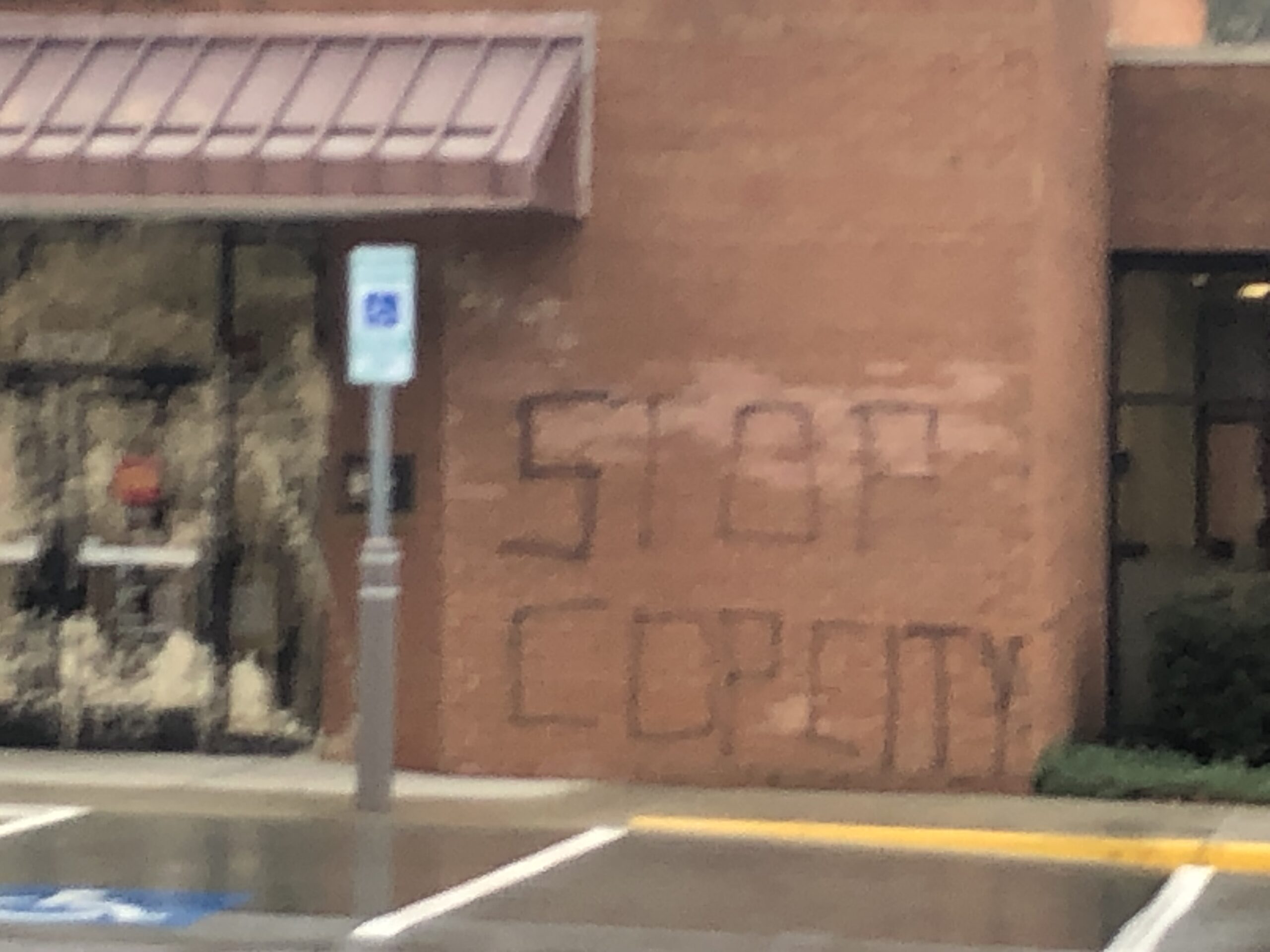 A brick wall next to a glass door with a Wells Fargo logo is tagged "STOP COP CITY" in black spray paint.