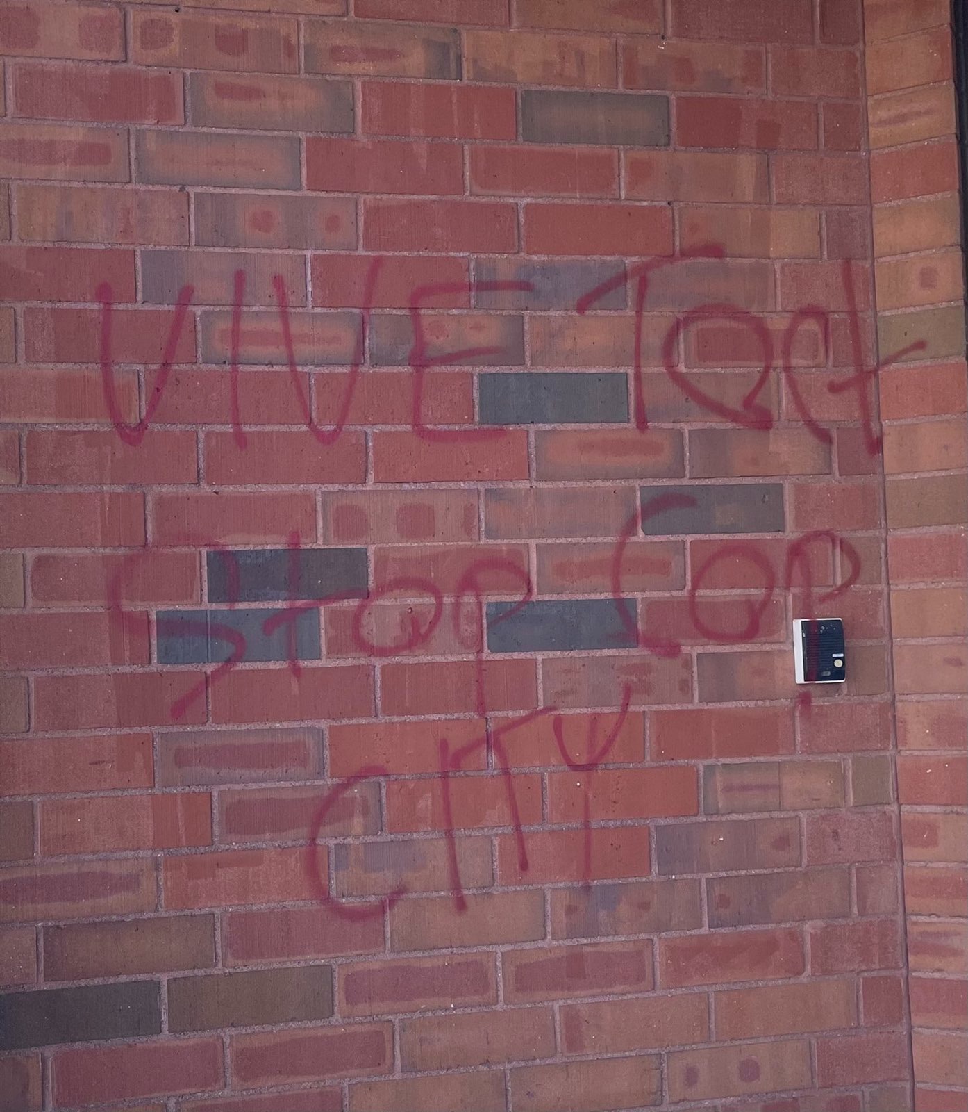 A brick wall with an intercom is tagged "VIVE TORT STOP COP CITY" in red spray paint.